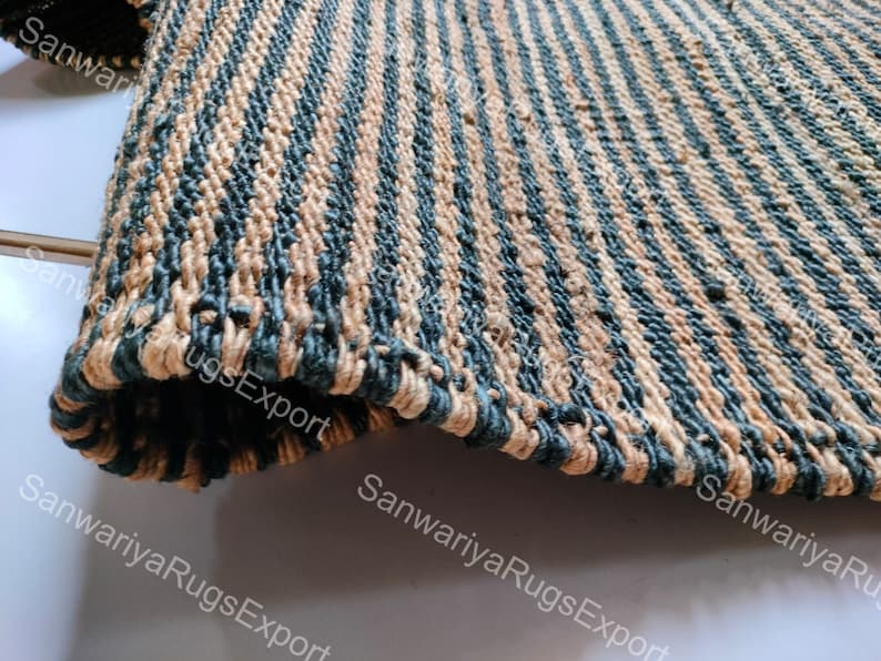 May include: A close-up of a woven rug with alternating stripes of tan and dark blue. The rug is made of natural fibres and has a rough texture.