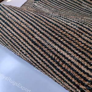 May include: Close-up of a woven rug with black and brown stripes. The rug is made of natural fibres and has a rough texture.