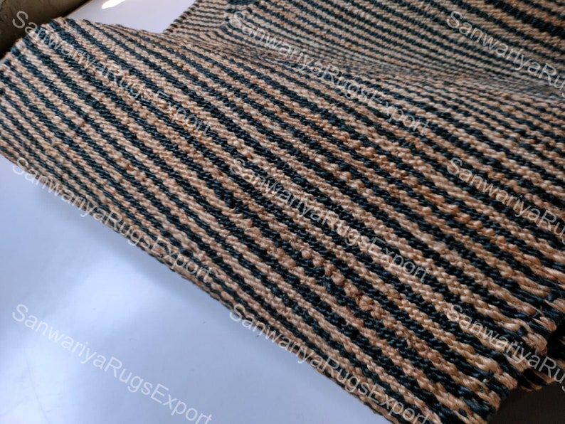 May include: Close-up of a woven rug with black and brown stripes. The rug is made of natural fibres and has a rough texture.