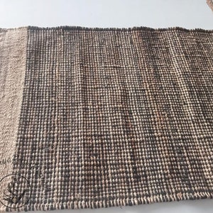 May include: A woven rug with a natural jute border and a dark brown center. The rug is made of natural fibers and has a textured surface.