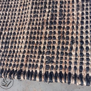 May include: A close-up of a black and natural jute rug with a woven pattern. The rug has a textured surface and is made of natural fibers.
