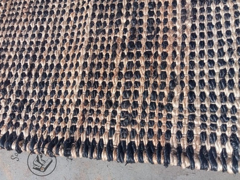 May include: A close-up of a black and natural jute rug with a woven pattern. The rug has a textured surface and is made of natural fibers.