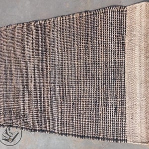 May include: A black and natural jute rug with a woven texture. The rug has a natural jute border.