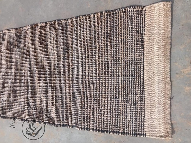 May include: A black and natural jute rug with a woven texture. The rug has a natural jute border.
