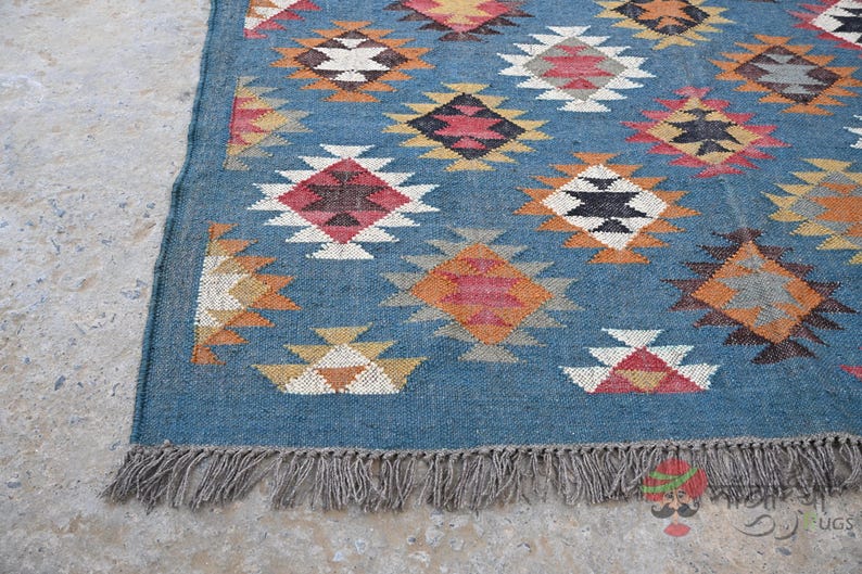 May include: A blue woven rug with a geometric pattern in shades of red, orange, white, and black. The rug has a fringe along the bottom edge and is likely made of natural fibers.