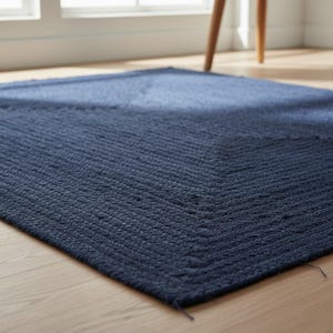 May include: A navy blue rectangular rug with a textured, woven design. The rug is placed on a light-coloured wooden floor. The rug's pattern features a chevron design.