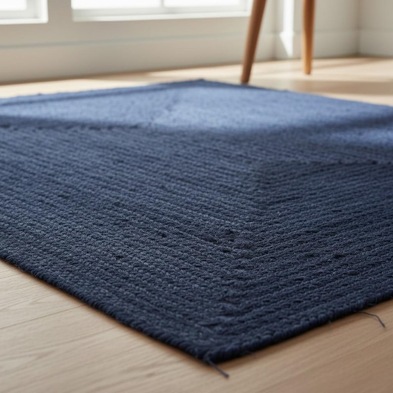 May include: A navy blue rectangular rug with a textured, woven design. The rug is placed on a light-coloured wooden floor. The rug's pattern features a chevron design.