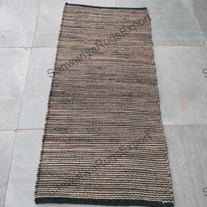 May include: A black and natural woven rug with a striped pattern. The rug is made of natural fibres and has a fringed edge.