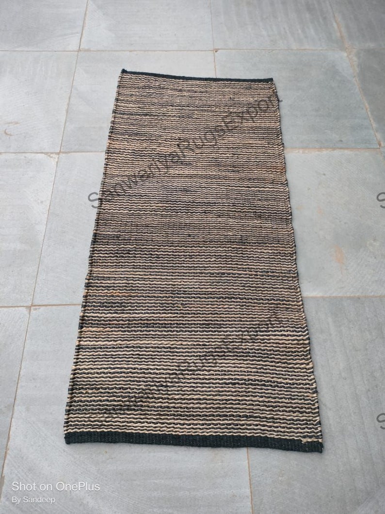 May include: A black and natural woven rug with a striped pattern. The rug is made of natural fibres and has a fringed edge.