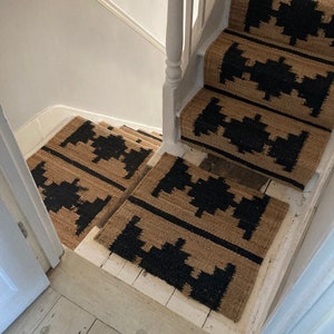 May include: A set of black and tan patterned stair treads. The treads are made of a woven material and have a geometric design.
