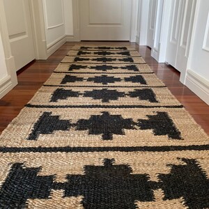 May include: A natural fibre rug with a geometric pattern in black and beige. The rug is woven with a textured surface and has a modern design.