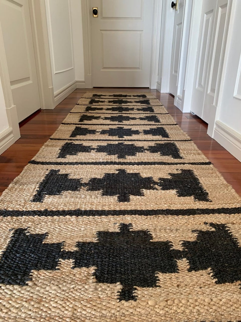 May include: A natural fibre rug with a geometric pattern in black and beige. The rug is woven with a textured surface and has a modern design.