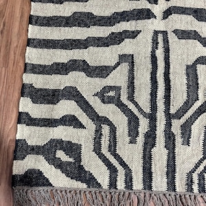 A close-up of a black and off-white zebra-patterned rug with fringe, showing the woven texture on a wooden floor.