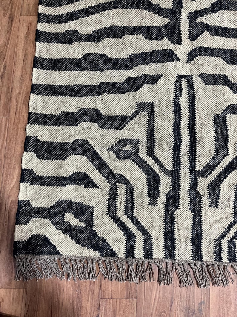 A close-up of a black and off-white zebra-patterned rug with fringe, showing the woven texture on a wooden floor.