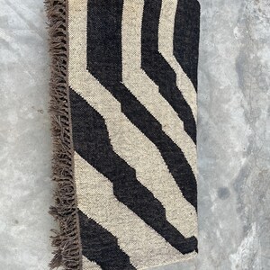 A black and off-white zebra-patterned rug with fringe is folded in half, lying on a concrete surface.
