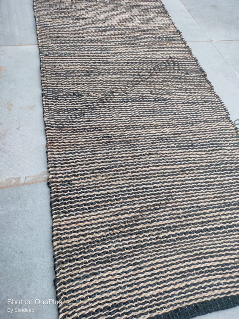 May include: A black and natural jute rug with a woven pattern. The rug has a textured surface and is made of natural fibres.