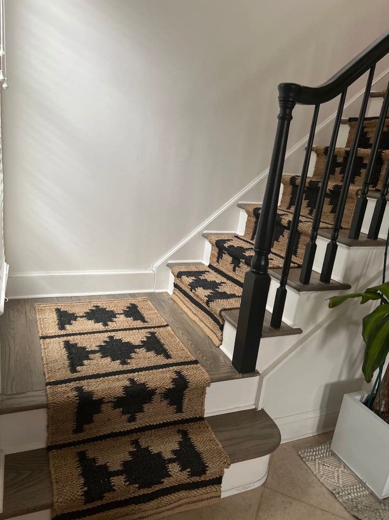 May include: A set of black and tan patterned stair treads with a black wooden handrail. The treads are made of a natural fibre material, possibly jute or sisal.