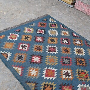 May include: A rectangular blue rug with a repeating geometric pattern of squares and diamonds in shades of orange, red, white, and black. The rug has a fringed edge.