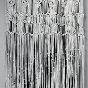 May include: White macrame curtain with intricate knotting patterns. The curtain features diamond and square designs, with vertical strands ending in small knots. A decorative and textured window treatment.