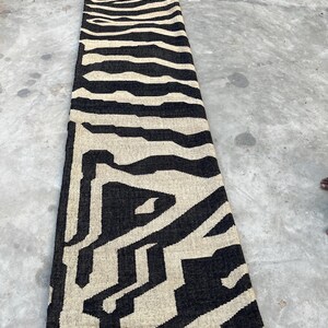 A long, narrow black and off-white zebra-patterned runner rug with fringe lies on a concrete floor.