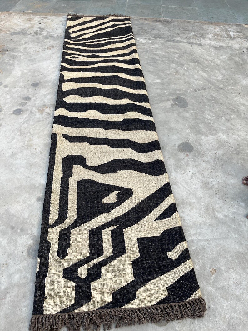 A long, narrow black and off-white zebra-patterned runner rug with fringe lies on a concrete floor.