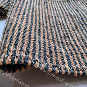 May include: Close-up of a striped rug made of natural fibres. The rug has alternating stripes of beige and dark blue. The rug is woven with a rough texture.
