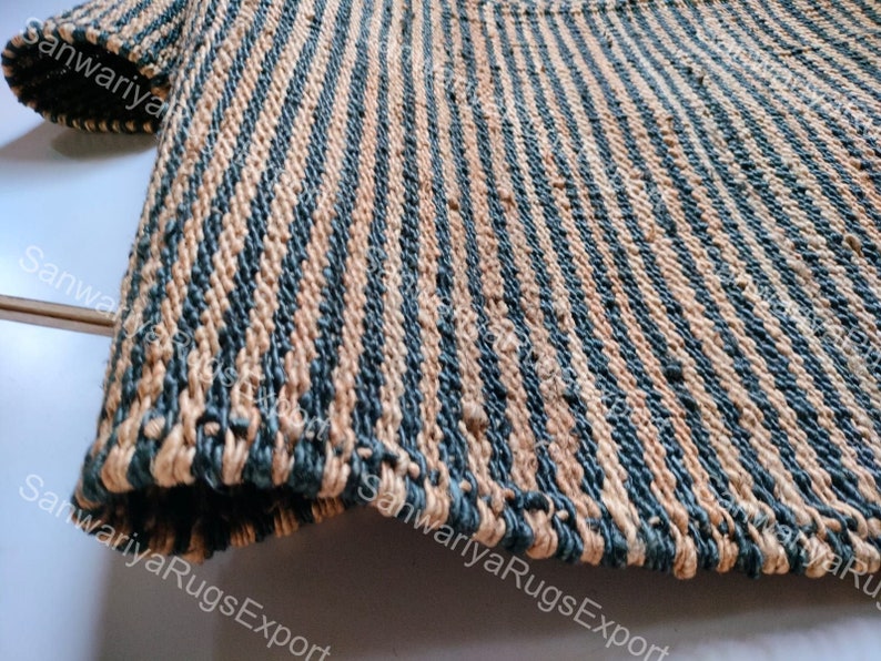 May include: Close-up of a striped rug made of natural fibres. The rug has alternating stripes of beige and dark blue. The rug is woven with a rough texture.