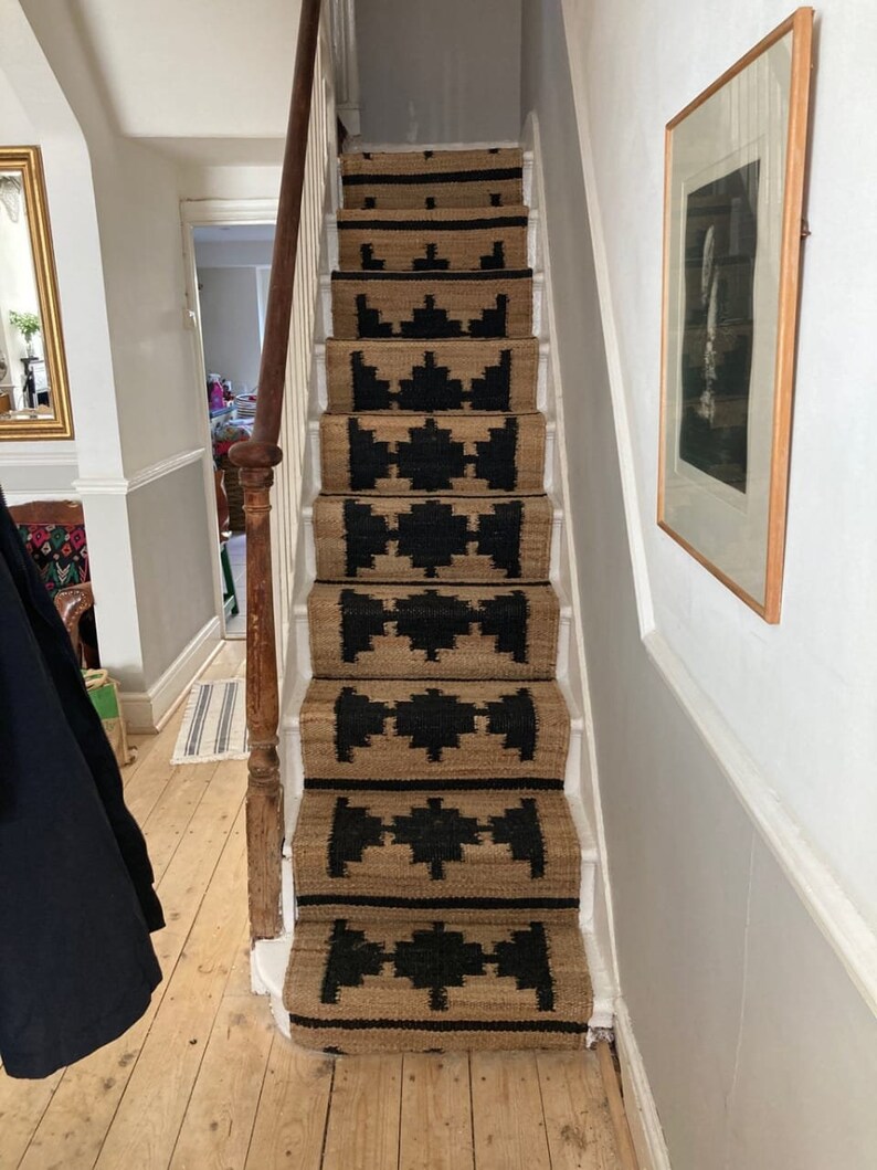 May include: A set of stair treads with a black and tan geometric pattern. The treads are made of a natural fibre material, such as jute or sisal.