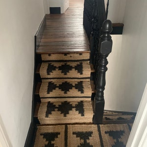 May include: A set of black and tan patterned stair treads with a black wooden handrail.