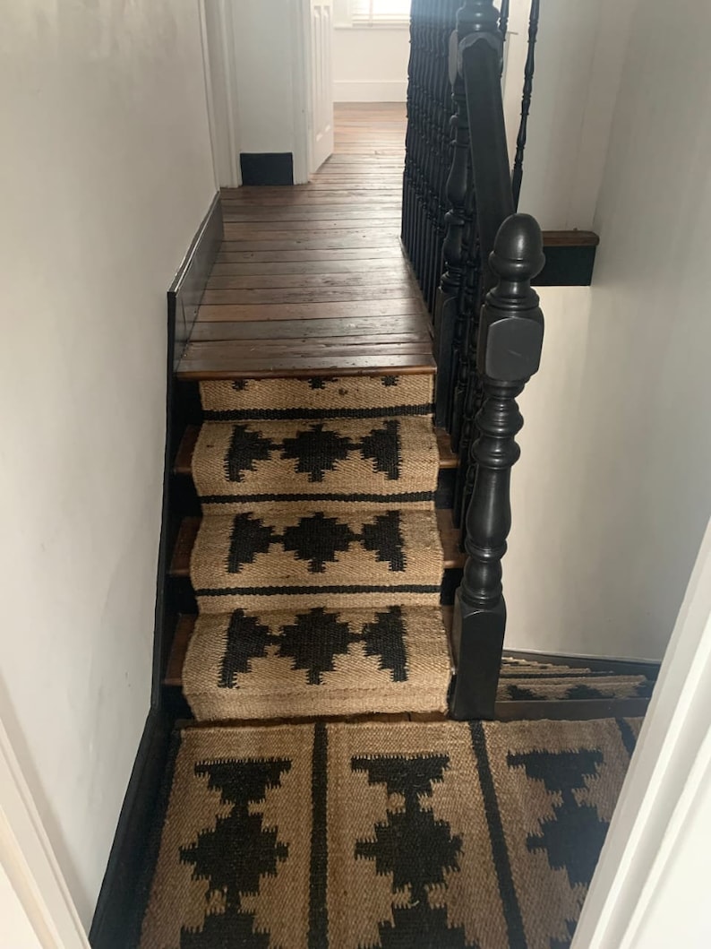 May include: A set of black and tan patterned stair treads with a black wooden handrail.