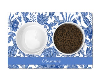 May include: A white ceramic pet bowl set with a blue and white floral design. The set includes two bowls and a matching mat with the name "Roxanne" printed on it.