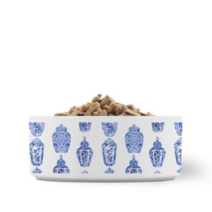 May include: A white ceramic pet bowl with a blue and white Chinoiserie design. The bowl is filled with dry pet food. The bowl's exterior features a repeating pattern of blue decorative jars and vases.