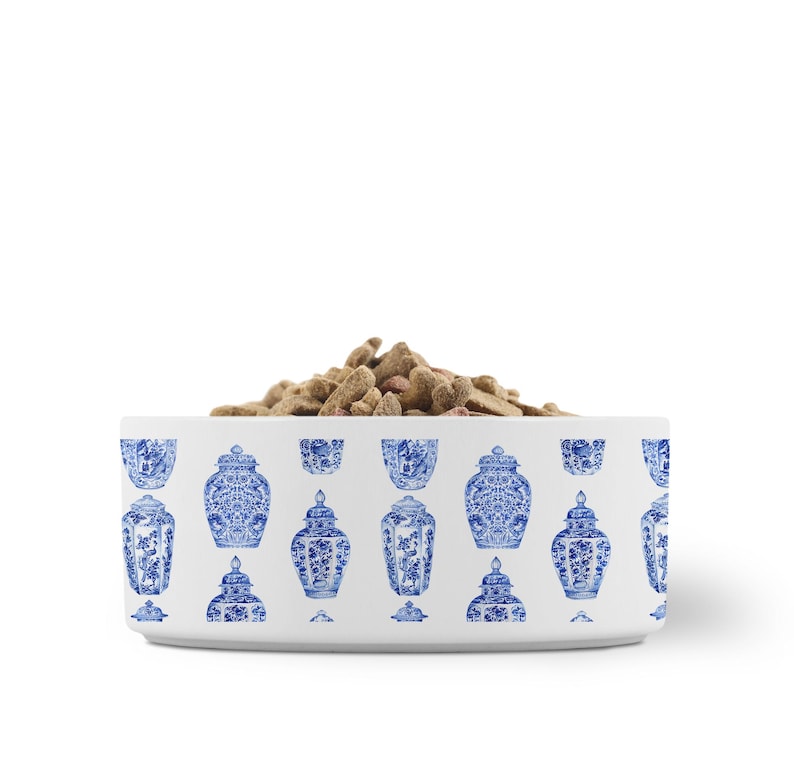 May include: A white ceramic pet bowl with a blue and white Chinoiserie design. The bowl is filled with dry pet food. The bowl's exterior features a repeating pattern of blue decorative jars and vases.