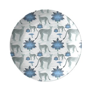 May include: A white ceramic plate with a blue and gray cheetah print pattern. The pattern features cheetahs, stylized trees, and blue flowers.