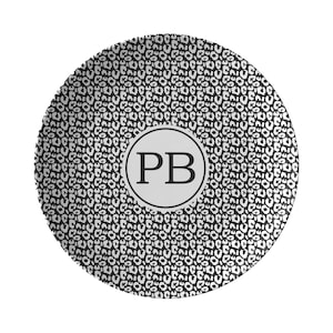 May include: A black and white leopard print ceramic plate with a white circle in the center. The circle has a black outline and the letters "PB" in black.