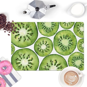 May include: A white rectangular kitchen mat with a repeating pattern of green kiwi fruit slices. The kiwi slices are painted in a watercolor style.
