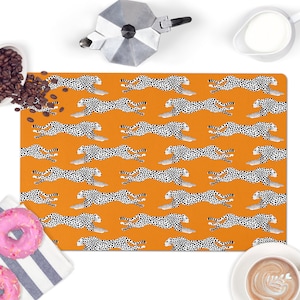 May include: Orange placemat with a repeating pattern of black and white cheetahs running.