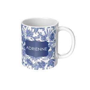 May include: White ceramic mug with a blue and white floral pattern. The name "Adrienne" is printed in a blue banner on the mug.