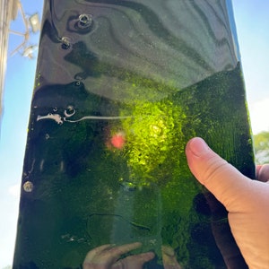 May include: A dark green glass sheet with a textured surface and a light green center. The glass is translucent and has a slight ripple effect.