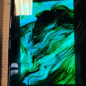 May include: A rectangular piece of glass with a black border and a swirling pattern of green and blue paint.