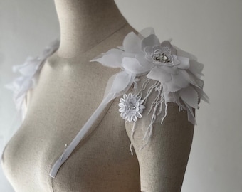 May include: White floral shoulder embellishments with delicate lace and beaded details. These embellishments can be used to add a touch of elegance to a wedding dress or other formal attire.