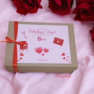 Può includere: Una scatola regalo di San Valentino con un nastro rosso. La scatola è decorata con cuori e la scritta "Happy Valentine's Day Box". Rose rosse sullo sfondo.