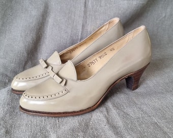 May include: A pair of beige leather heeled shoes with a bow detail. The shoes have a pointed toe and a low heel. The size is marked as 4½ and the number 27577 9522 is printed on the sole.
