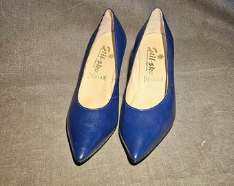 Puede incluir: Par de zapatos de salón de punta azul marino con tacón bajo. Los zapatos tienen una etiqueta dorada en el interior que dice "Stil-ste Design".