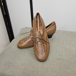 May include: A pair of brown leather lace-up shoes with a woven pattern on the toe. The shoes have a low heel and are made of a soft, supple leather.