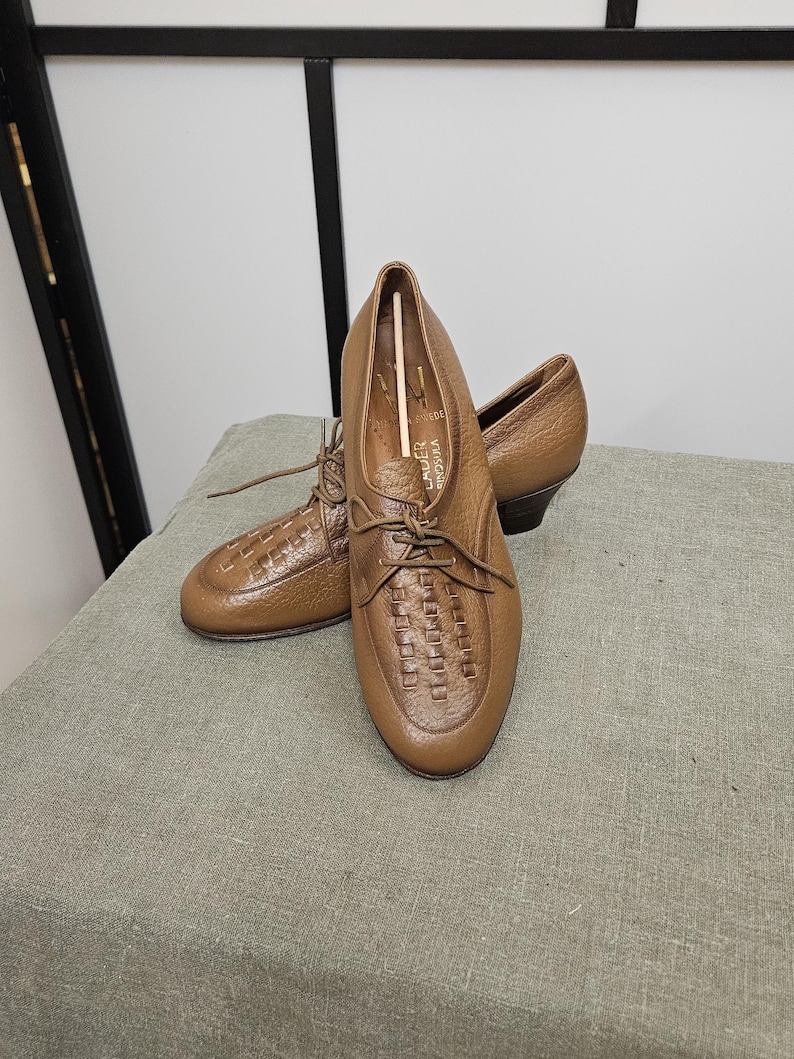 May include: A pair of brown leather lace-up shoes with a woven pattern on the toe. The shoes have a low heel and are made of a soft, supple leather.