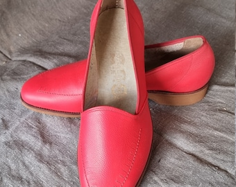 Puede incluir: Un par de zapatillas de cuero rojo brillante con punta puntiaguda y un diseño cosido. Las zapatillas tienen una suela de cuero marrón.