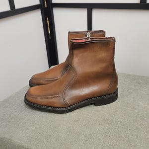 Peut inclure: Une paire de bottines en cuir marron avec une fermeture éclair sur le côté. Les bottes ont un détail cousu sur la pointe et une semelle en caoutchouc noir.