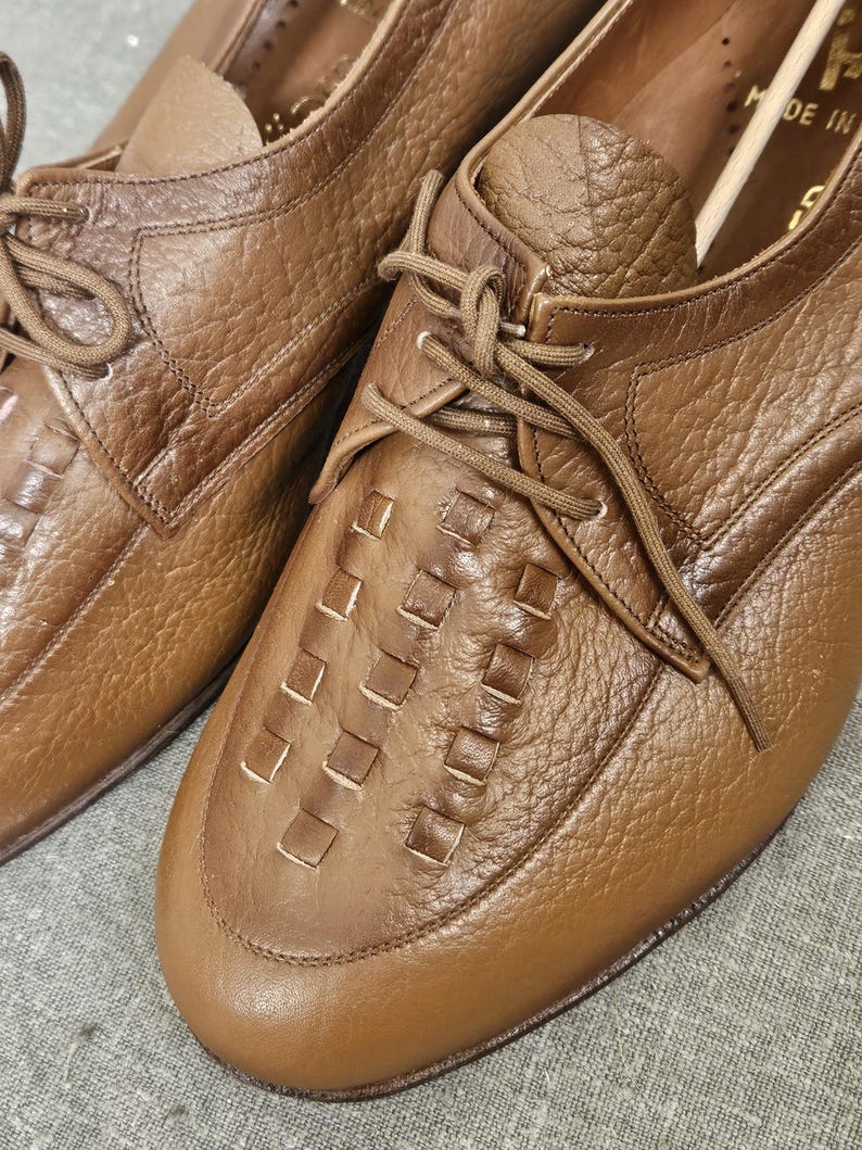 May include: A pair of brown leather lace-up shoes with a woven pattern on the toe. The shoes have a classic design and are made of high-quality leather.