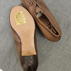 May include: A pair of brown leather shoes with laces. The shoes have a label on the sole that reads "AS HI 30" and "G. LIDER,  TANGUIA".